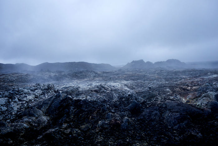 The image depicts a rocky area with fog, resembling a moon surface, in an outdoor landscape. The sky is overcast with clouds, and there is a wintry feel. The scene is reminiscent of a cold, desolate environment, located in Iceland.