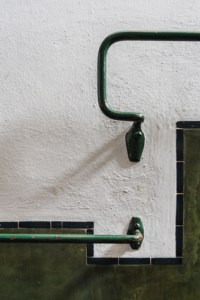 The photograph captures a pair of metal handles securely affixed to a wall, serving as an integral part of an art deco-inspired wall decoration, strategically positioned near a staircase. Exhibiting an aged charm, these handles bear the visible marks of time, attesting to their enduring utility over the years.