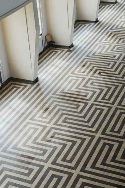 A black and white floor adorned in art deco style unfolds, showcasing the timeless elegance of geometric patterns. Each meticulously arranged tile tells a story of meticulous craftsmanship, creating a visual masterpiece. Amidst this monochromatic symphony, a solitary chair in the corner adds a touch of contemplative solitude, contributing to the overall allure of this captivating space.